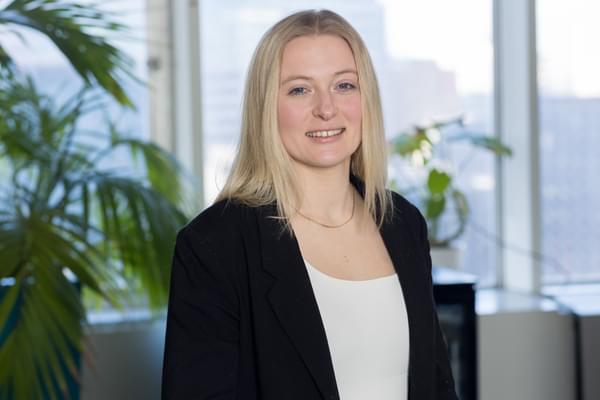 Professional headshot of Amy in the Scaramanga offices. She is wearing a white top, black blazer, and has short blond hair.