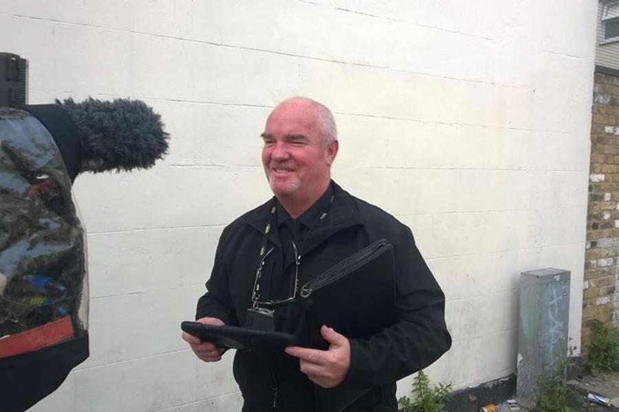 Man smiling, standing in front of a filming camera