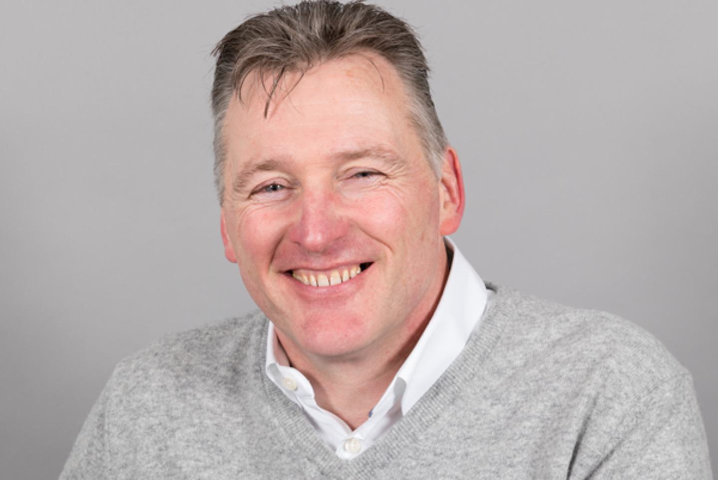 Professional photo of Bob Dickinson wearing a grey polo sweater and collared shirt.