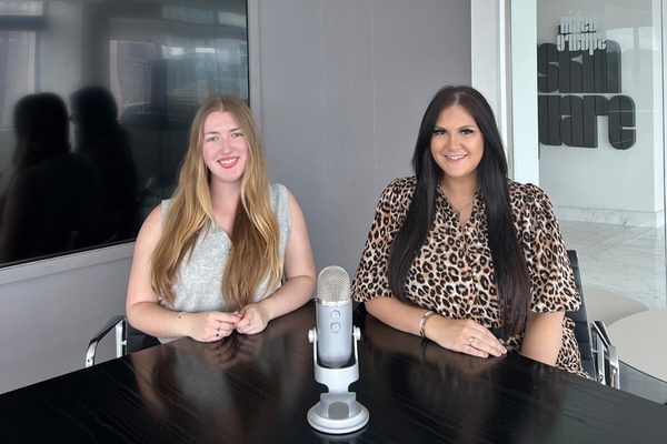 Emma and Charlotte sat at a table in front of a microphone recording the podcast episode.