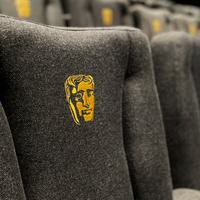 Multiple rows of cinema seats blurring into the distance. Each seat contains the BAFTA mask emblem.