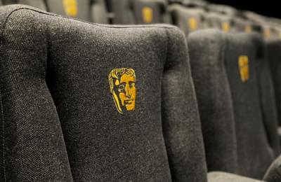 Multiple rows of cinema seats blurring into the distance. Each seat contains the BAFTA mask emblem.