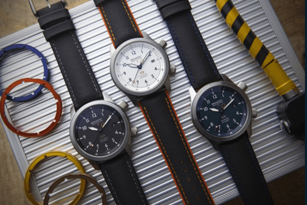 A selection of 3 watches from Bremont MB range, displayed alongside components like the coloured bezels and straps. The viewpoint is from above with the items placed on a steel box.