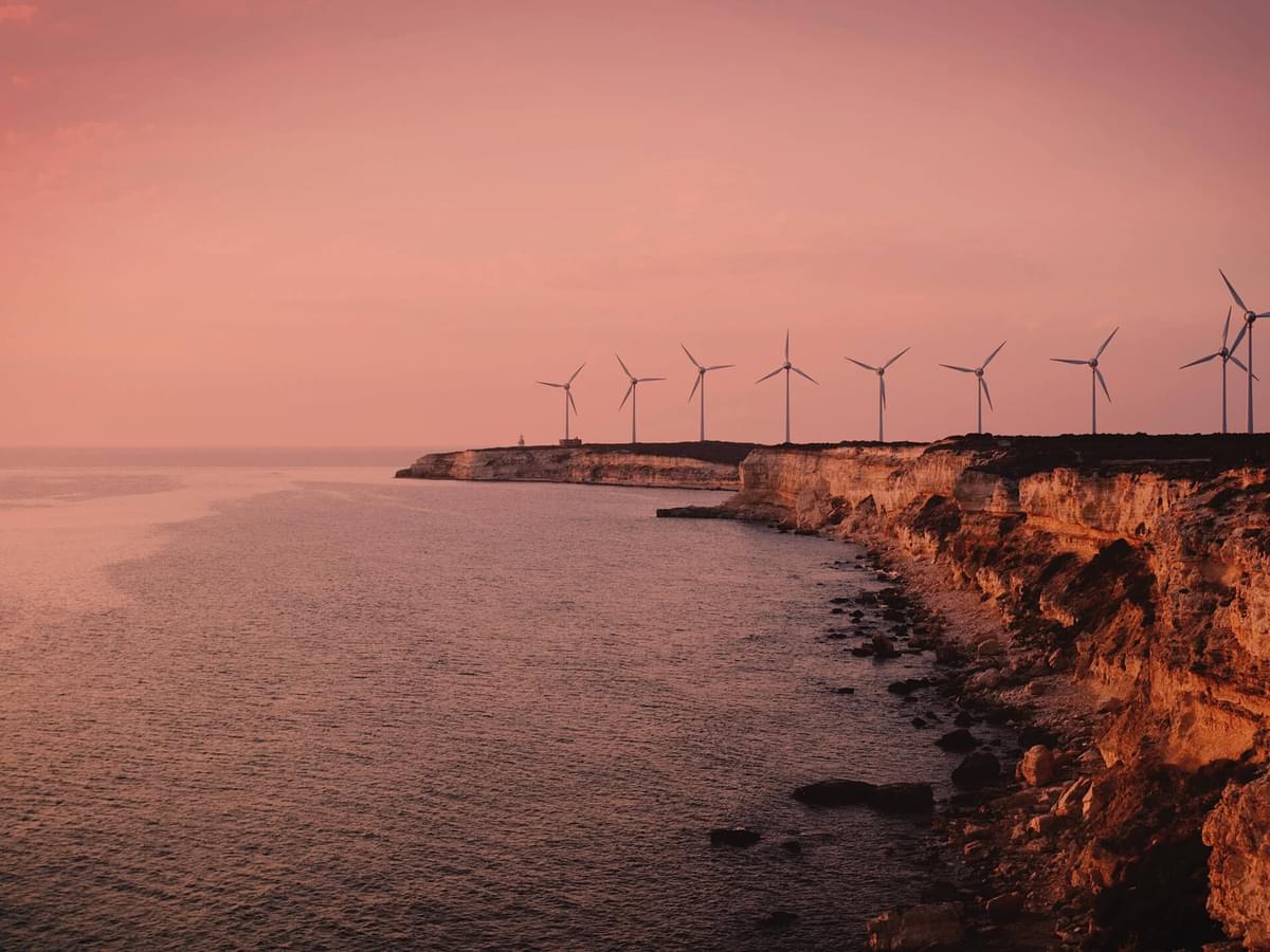 A scenic image of a cliff front lined with wind turbines overlooking the sea. The image has a sepia tone making it feel warm and nostalgic.