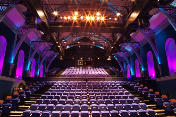 With a central viewport from the stage, the many rows of chairs rise up the Corn Exchange Auditorium with the alcoved walls beautifully lit in blue and purple to make the space look really dramatic.