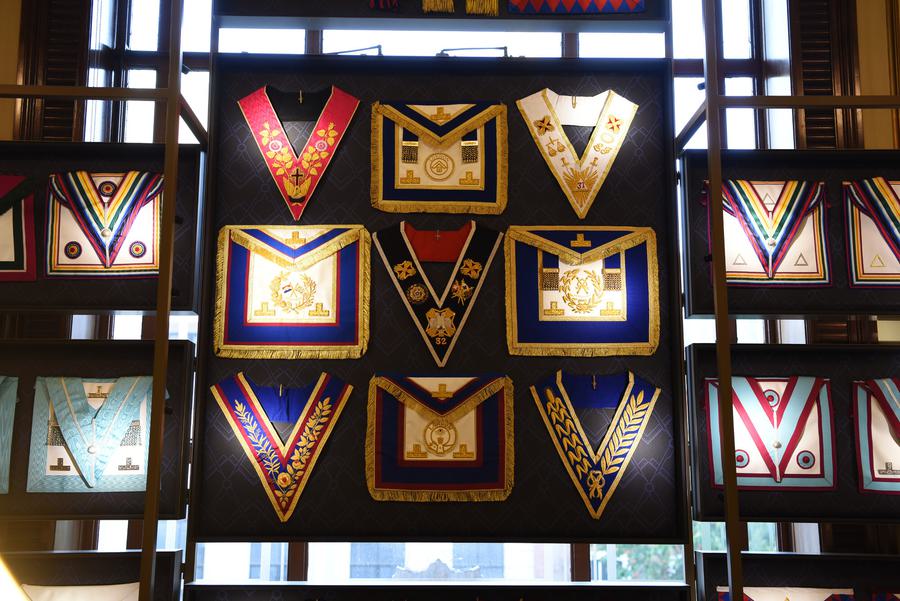 A collection of mason sashes and aprons on display in a display case