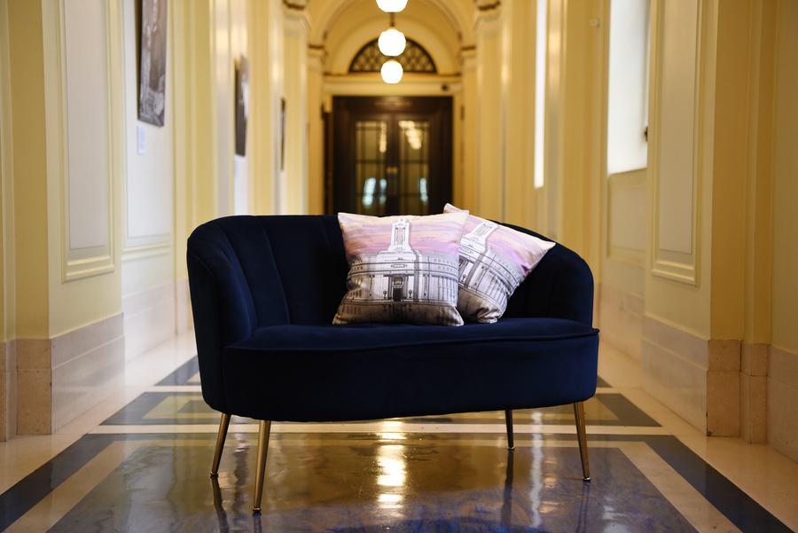 A blue two seater sofa with pillows on depicting The Freemans Hall in London. The sofa is in a long hallway that is brightly lit.