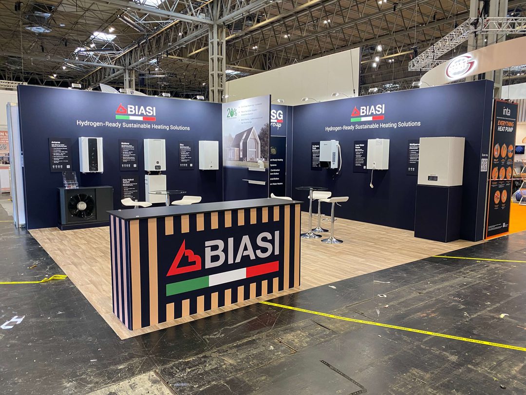 Alternate angle of the Biasi stand, this time without anyone inside of it. Biasi front desk at the forefront of the picture with biasi on the walls of the stand and flooring in the stand area.
